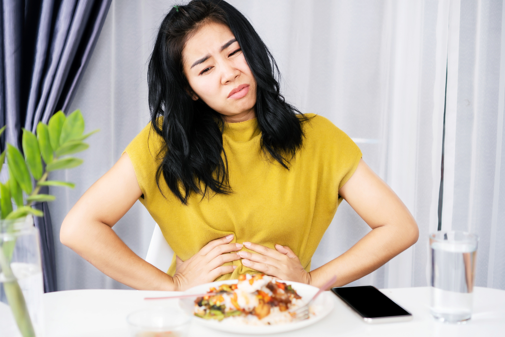 Asian woman suffering from stomachache, GERD after eating spicy food hand holding her pain stomach